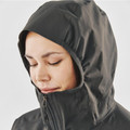 Woman wearing charcoal technical shell jacket with structured hood, ribbed facing, and centre-front zip detail