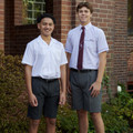 Two male students wearing charcoal grey single pleat formal shorts with white short-sleeve shirts outdoors