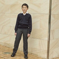 Boy wearing charcoal grey school trousers with ribbed waistband, styled with navy v-neck jumper and white shirt
