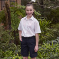Child wearing white short sleeve button-up blouse with point collar, styled with navy shorts in garden setting