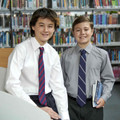 Two students in white and silver-grey no-iron long sleeve shirts with button-up collars and ties in a school library