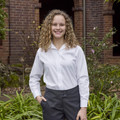 Young woman wearing a white long sleeve blouse with revere collar and button front, styled with charcoal trousers outdoors