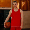 Male model wearing red reversible basketball singlet with white side panels, holding a basketball on an indoor court