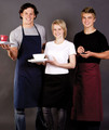 Three hospitality staff wearing navy full bib, black waist, and burgundy waist aprons in a café service setting