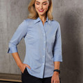 Woman wearing a pale blue chambray button-up shirt with three-quarter sleeves and pointed collar
