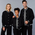 Two adults and a child wearing black varsity jackets with white contrast stripe ribbed cuffs, collar and hem, snap button front closure