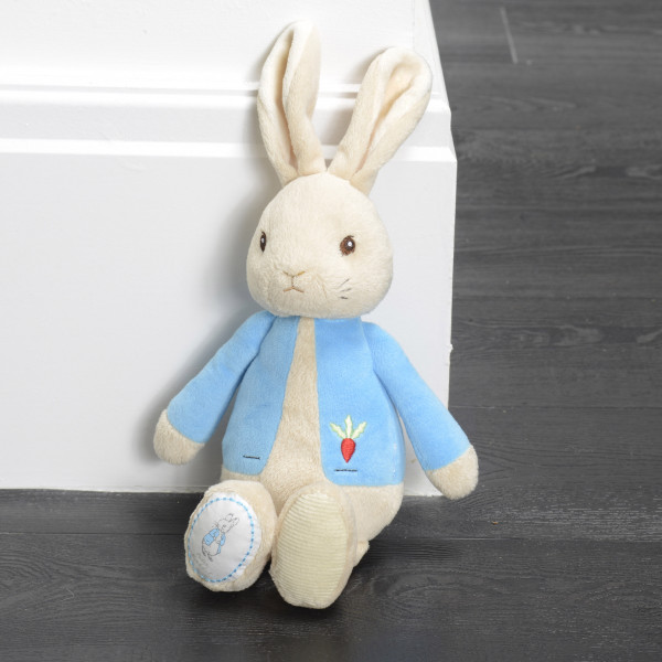 Cream plush rabbit toy wearing light blue jacket with embroidered detail, seated against white background