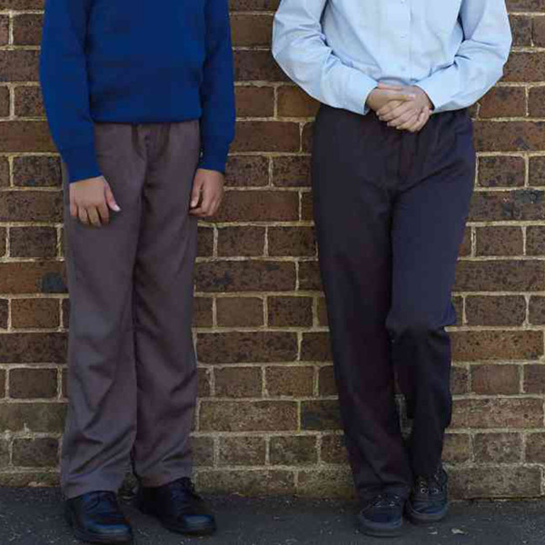 Two students wearing charcoal grey and navy long school pants against brick wall