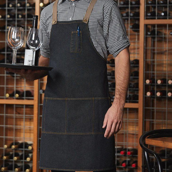 Black denim bib apron with contrast stitching, chest pocket, and tiered front pockets worn over checkered shirt
