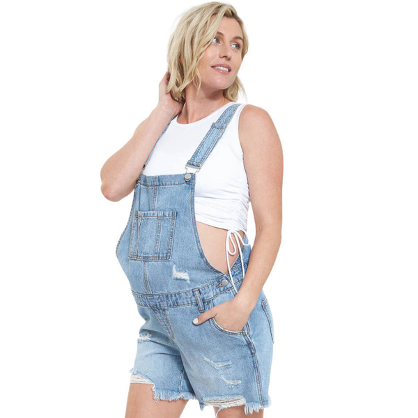 Pregnant model wearing pale blue distressed denim short overalls with frayed hem and adjustable straps