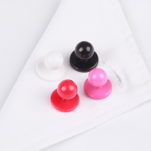 Four chef coat snap buttons in white, black, red, and hot pink resting on white fabric collar
