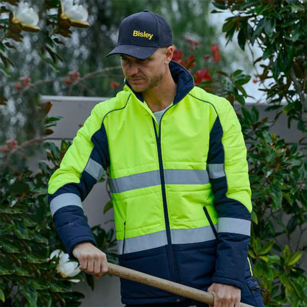 Man working outdoors in yellow and navy hi vis puffer jacket with reflective tape panels and full-length zip