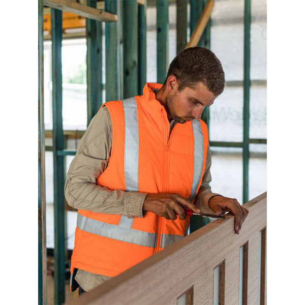 Man on construction site wearing hi vis orange puffer vest with silver reflective X-back tape and zip front