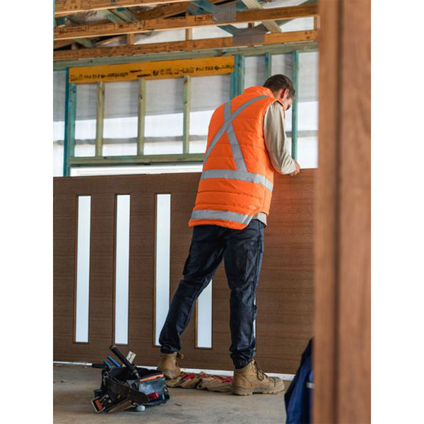 Tradie wearing orange hi vis puffer vest with reflective X back tape on an active construction site