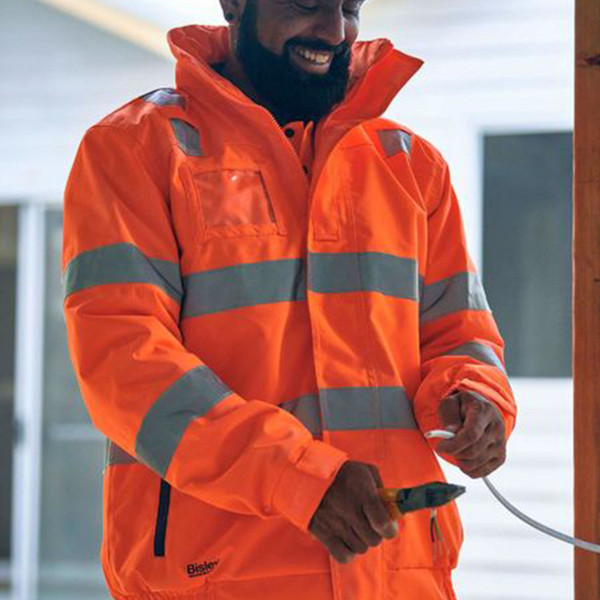 Man wearing orange hi-vis bomber jacket with silver reflective tape bands and high collar on worksite