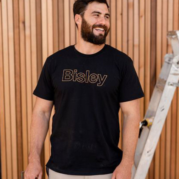 Man wearing black cotton crew neck tee with gold outline Bisley chest print, styled in a workshop setting