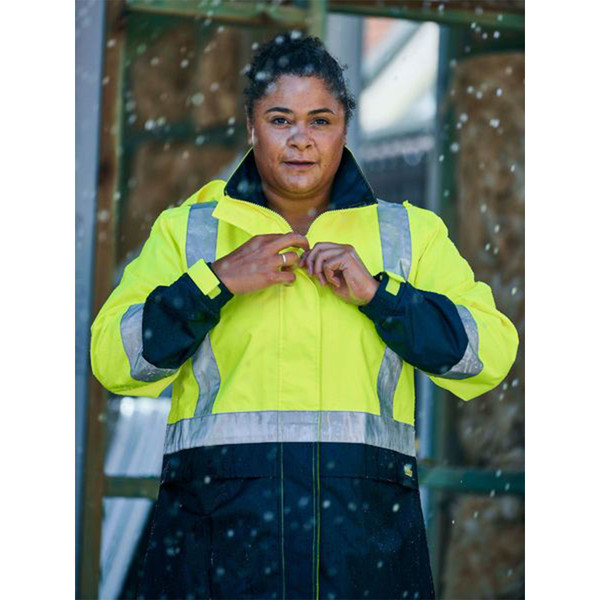 Woman fastening a hi vis yellow and navy two-tone rain jacket with reflective tape in snowy outdoor conditions