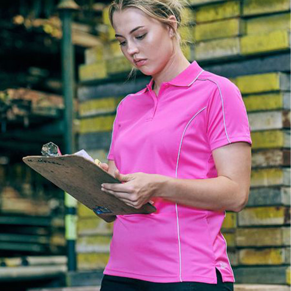 Woman in hot pink performance polo with white reflective piping reviewing clipboard in warehouse setting
