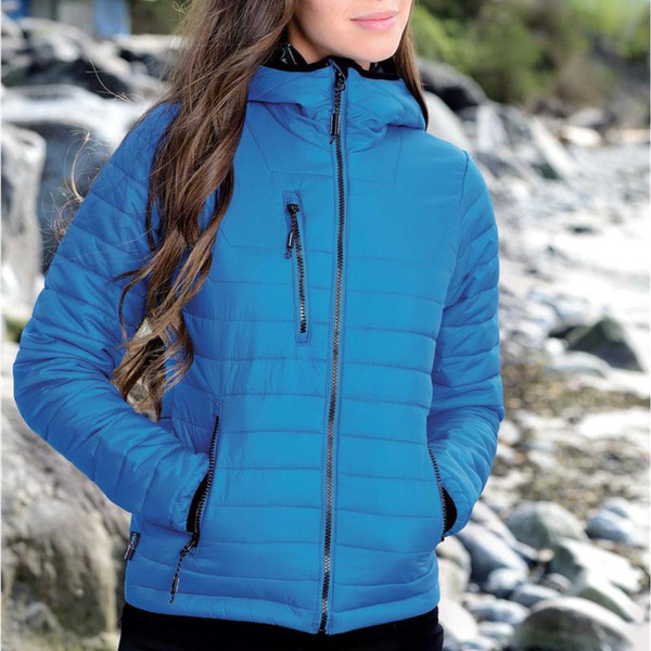 Woman wearing cobalt blue lightweight puffer jacket with hood, contrast zip details and quilted panels, rocky coastal backdrop