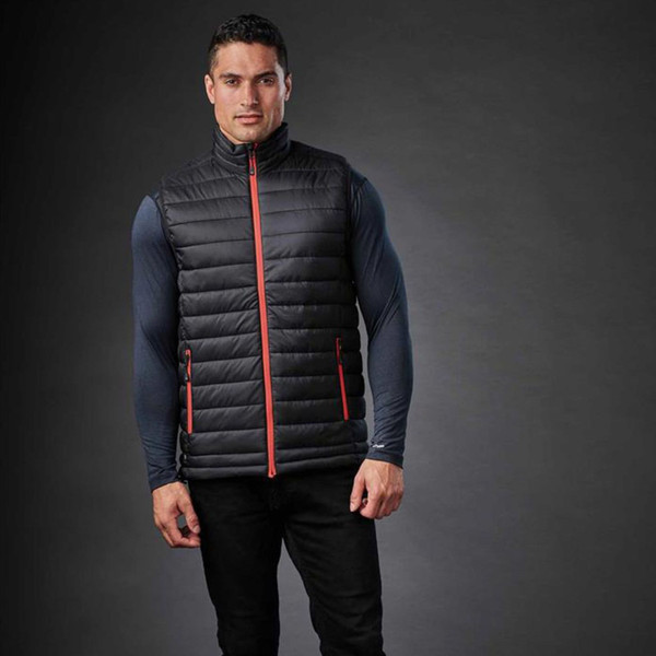 Man wearing charcoal quilted insulated vest with coral red contrast zip and side zip pockets