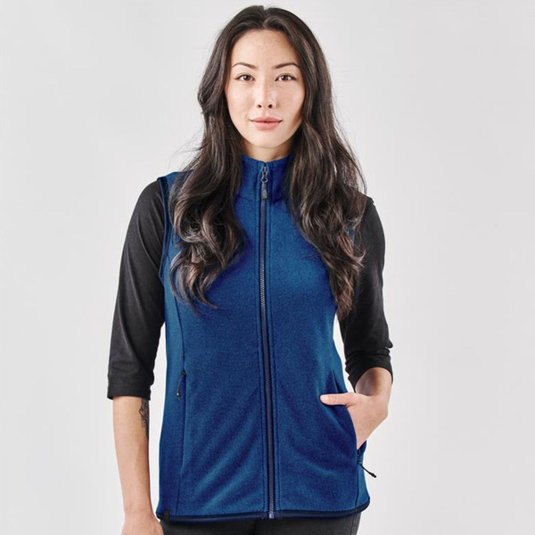 Woman wearing a heathered navy blue full-zip fleece vest with zip pockets and a stand collar