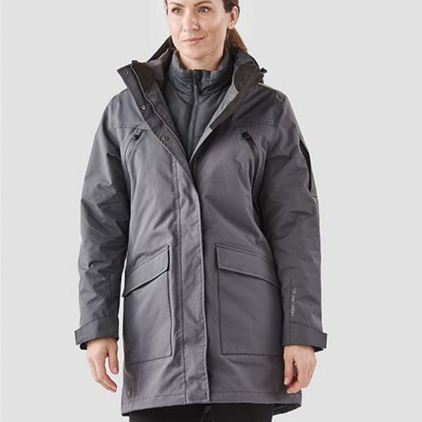Woman wearing charcoal grey long waterproof system jacket with black inner vest, zip chest pocket and large flap hip pockets