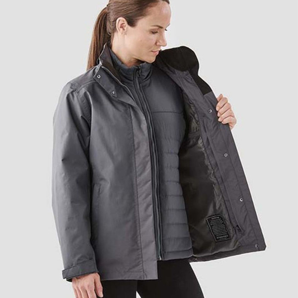 Woman opening graphite grey Stormtech system jacket revealing quilted black insulated inner layer with zip-out construction