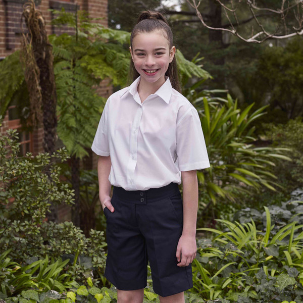 Girl wearing navy formal school shorts with front pockets and white short-sleeve shirt, outdoor garden setting