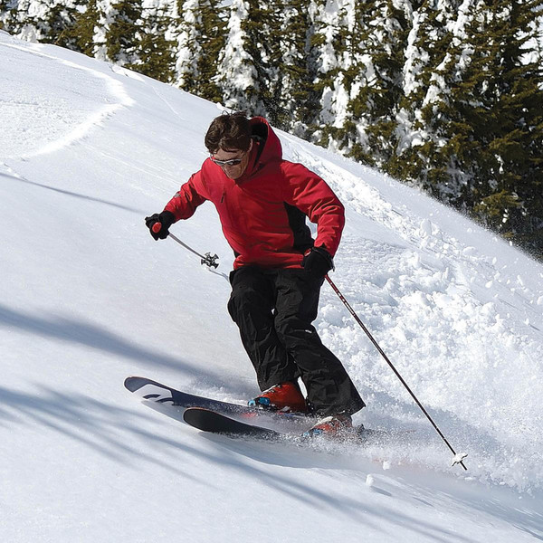 Red waterproof system jacket with hood worn skiing in snowy mountain conditions