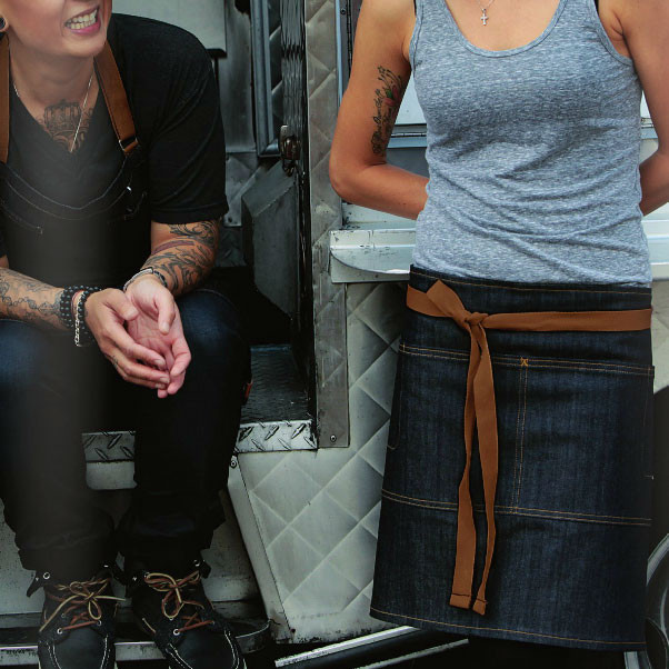 Denim waist apron with tan contrast ties and divided pockets worn over dark jeans