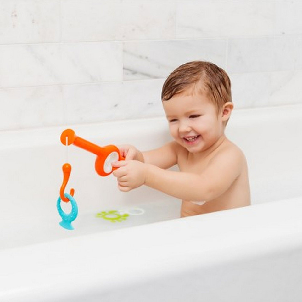 Child playing with orange and teal fishing pole bath toy with magnetic attachments in bathtub