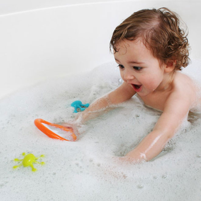 Colourful floating bath toys with orange net and green, blue bug shapes in soapy water