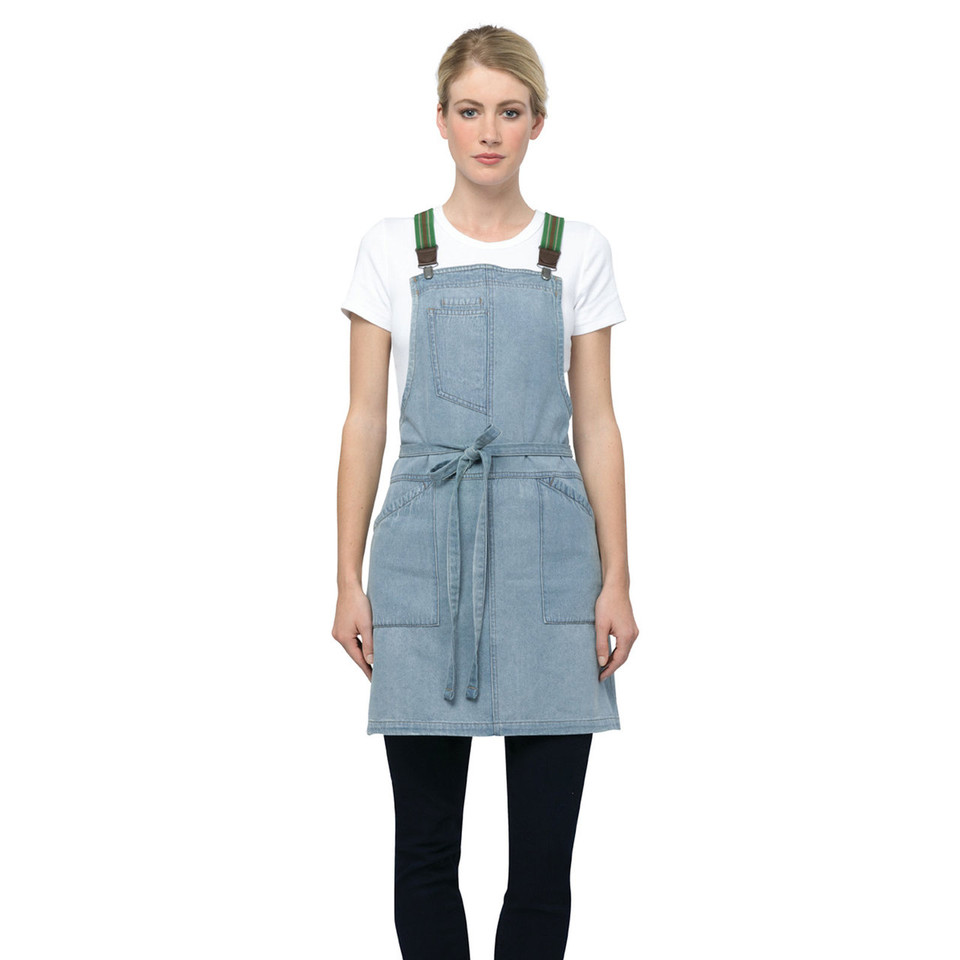 Sky blue denim-style bib apron with forest green adjustable straps, front pockets, and waist ties over white tee and black pants