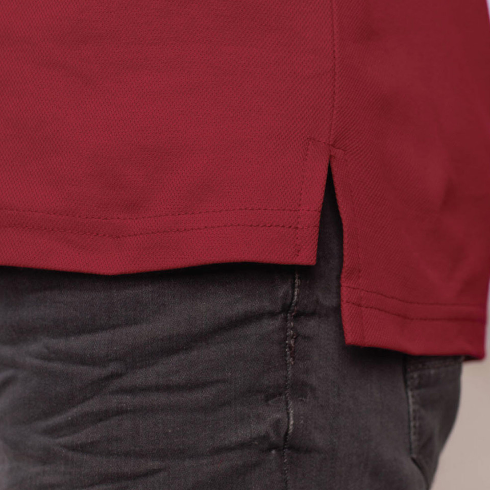 Close-up of crimson red long sleeve polo hem with side vents and clean double-needle stitching on model