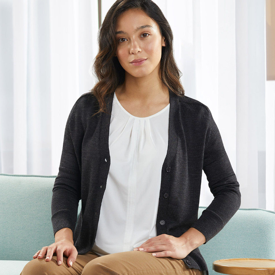Woman seated wearing a charcoal marle merino wool V-neck cardigan with button front over a white top