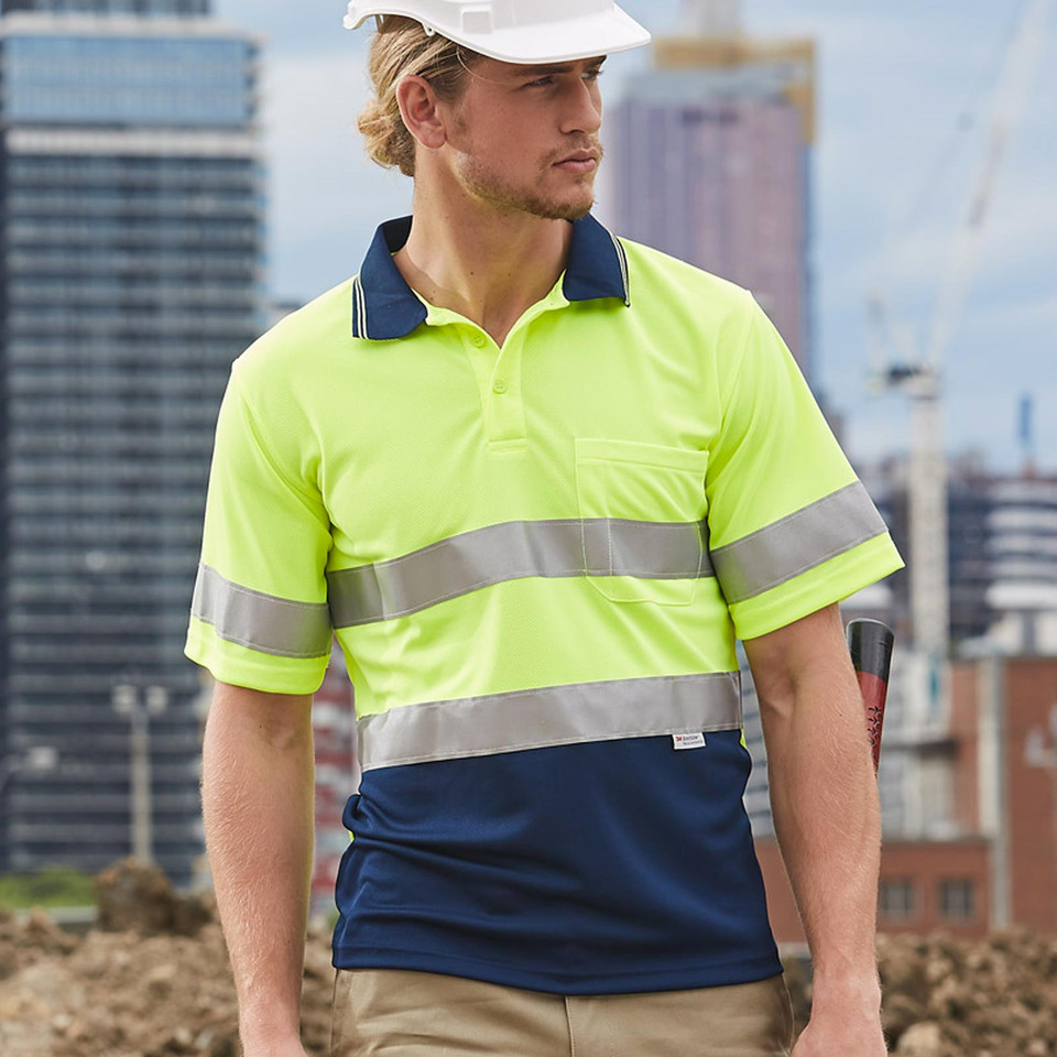 Man on construction site wearing hi-vis yellow and navy two-tone polo with silver reflective tape bands