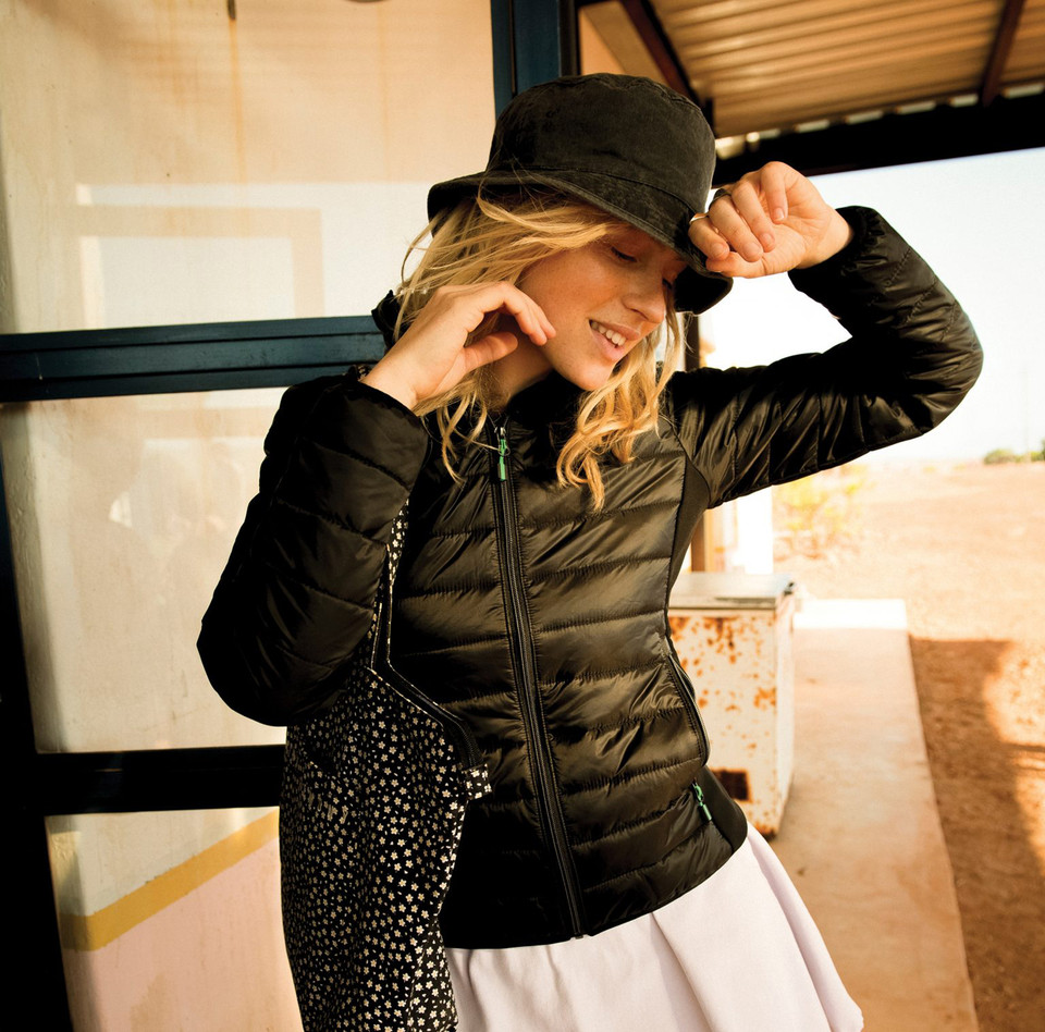 Woman wearing black lightweight puffer jacket with centre zip and green zip pulls, fitted silhouette, outdoor setting