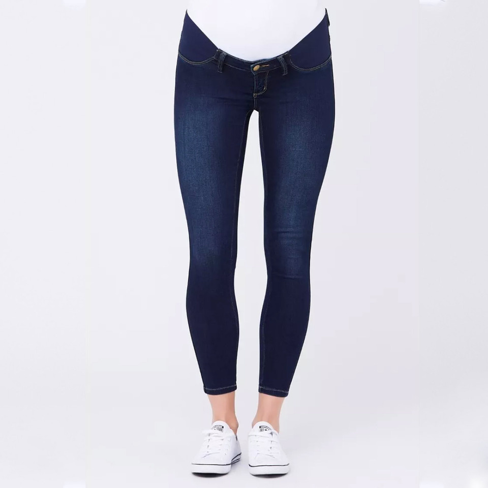 Dark indigo maternity jeggings with under-bump panel and gold-tone button, cropped ankle length, worn with white sneakers
