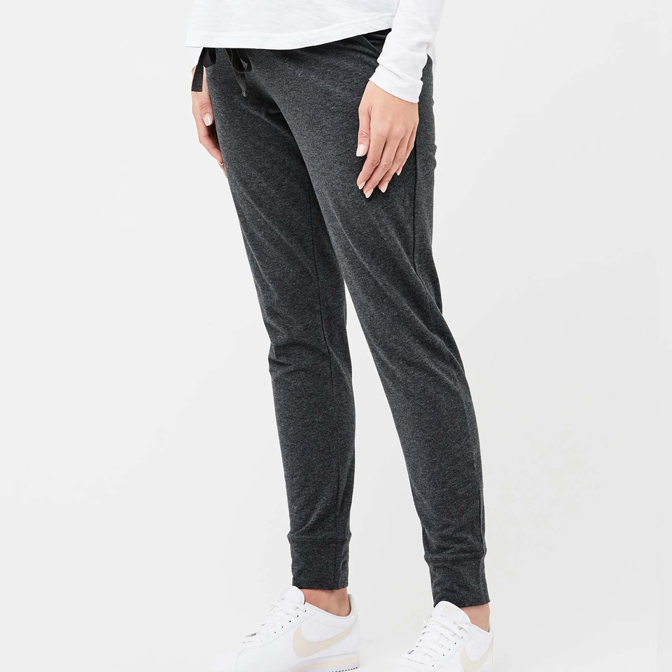 Charcoal grey maternity joggers with fitted ankle cuffs and adjustable waistband worn with white sneakers