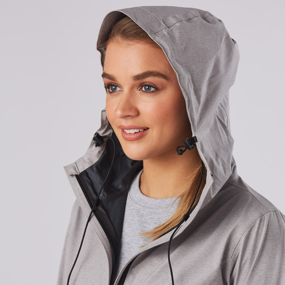 Woman wearing silver-grey waterproof jacket with adjustable hood, black chin guard panel and drawcord detail