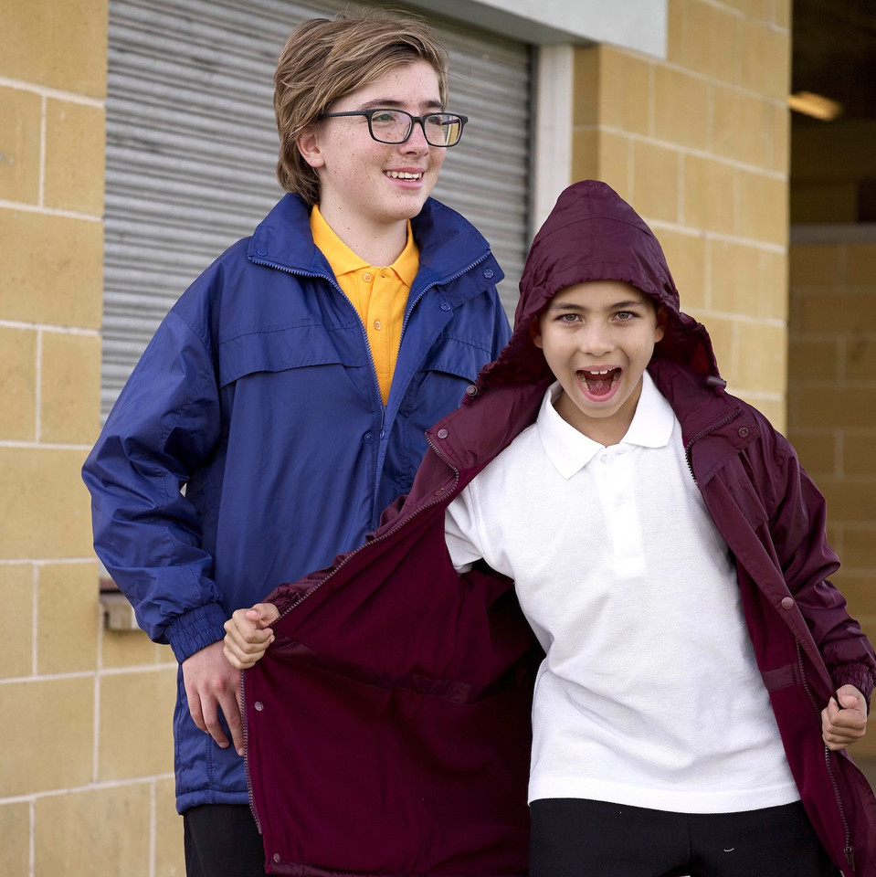Two kids wearing navy and maroon all-weather jackets with hoods, styled over school uniforms outdoors