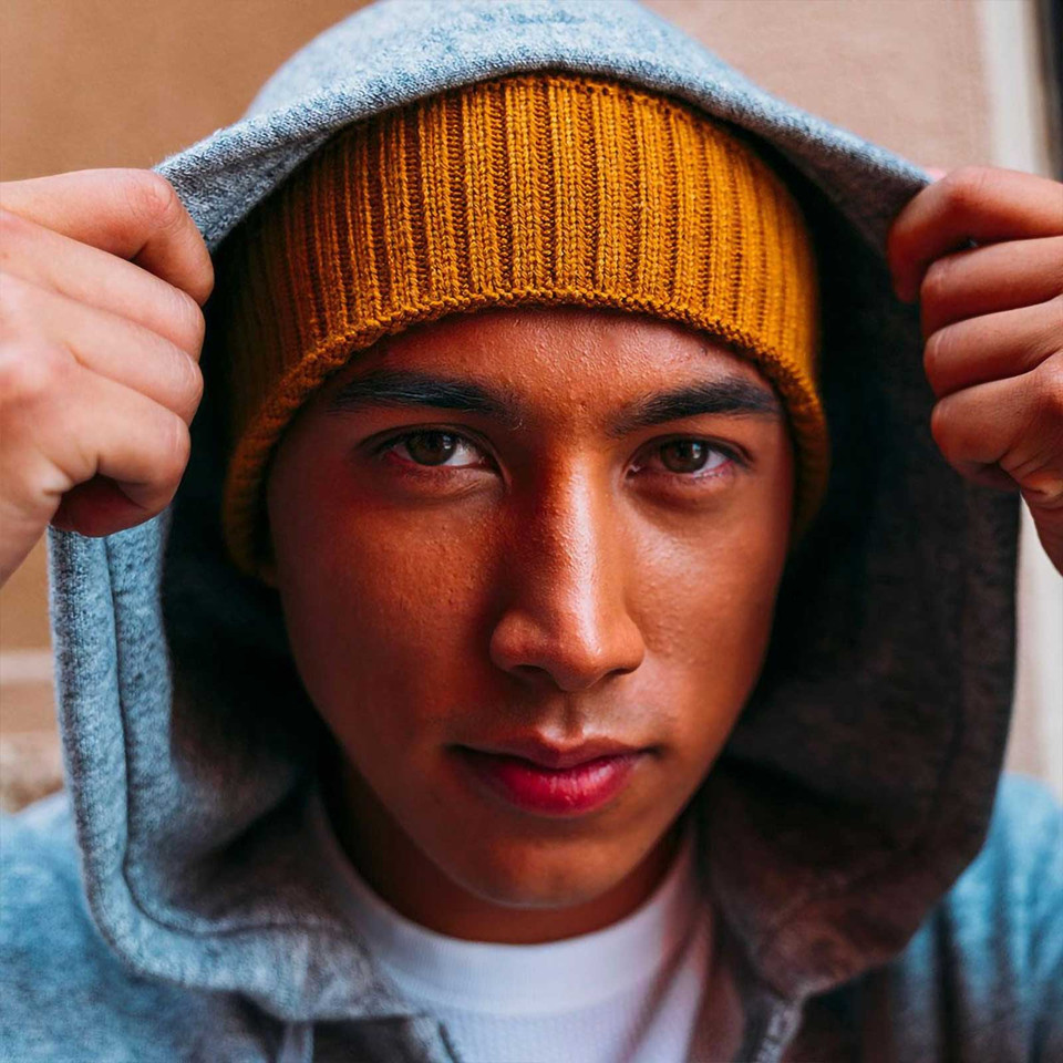 Mustard ribbed cuff beanie worn with charcoal hood, showing textured knit detail and fold-up design