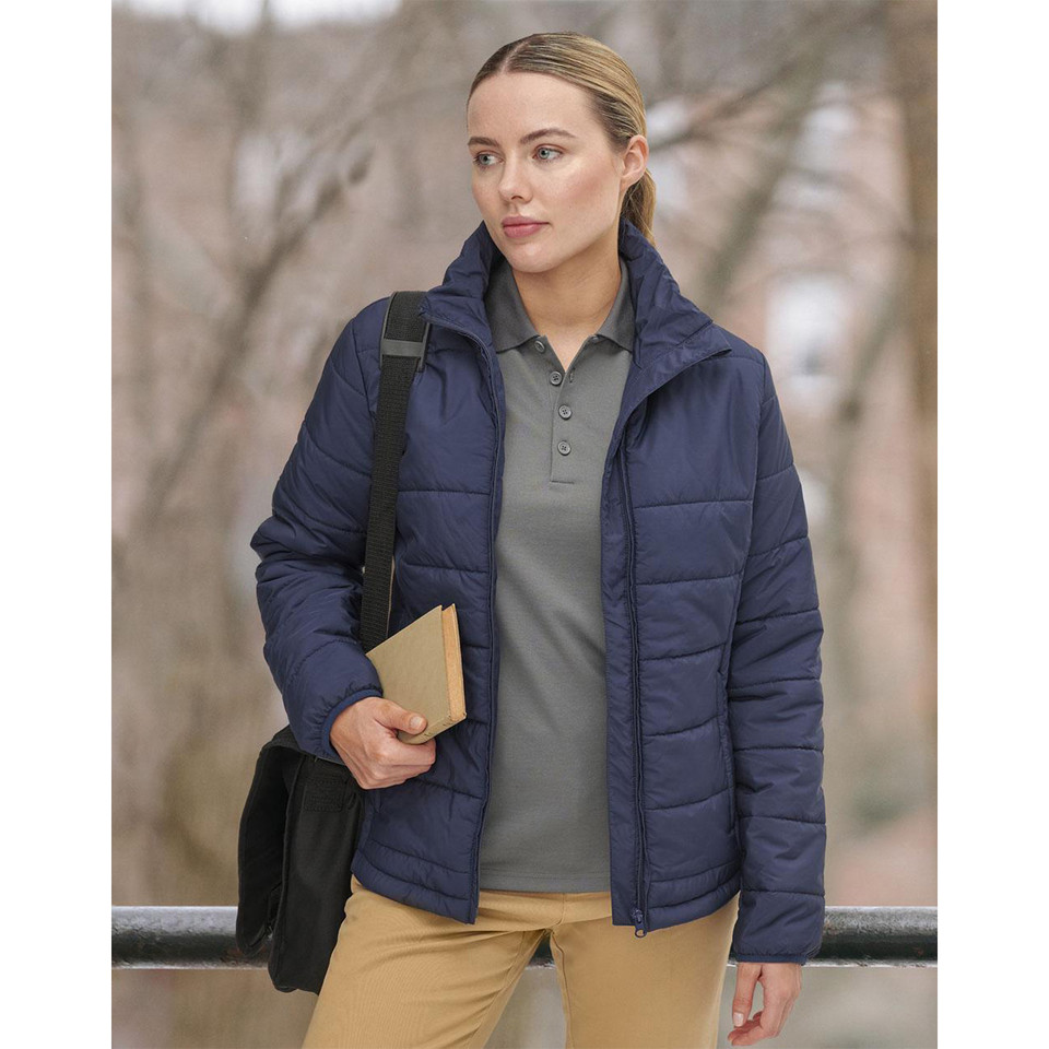 Woman wearing navy quilted puffer jacket with hood, front zip, and horizontal baffle panels, styled with grey polo and tan trousers