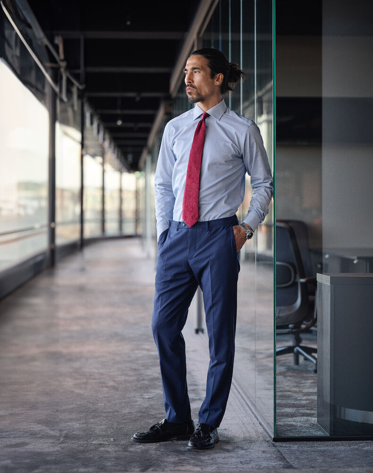 Man in corporate setting wearing light blue no-wrinkle long sleeve dress shirt with red tie and navy trousers
