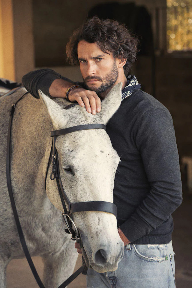 Navy organic cotton v-neck sweater with ribbed collar and cuffs worn by model with white horse