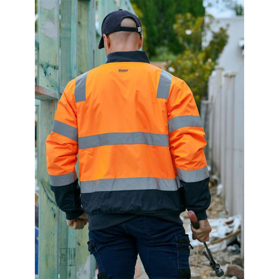 Man on worksite wearing orange and navy hi-vis bomber jacket with silver reflective tape bands across back