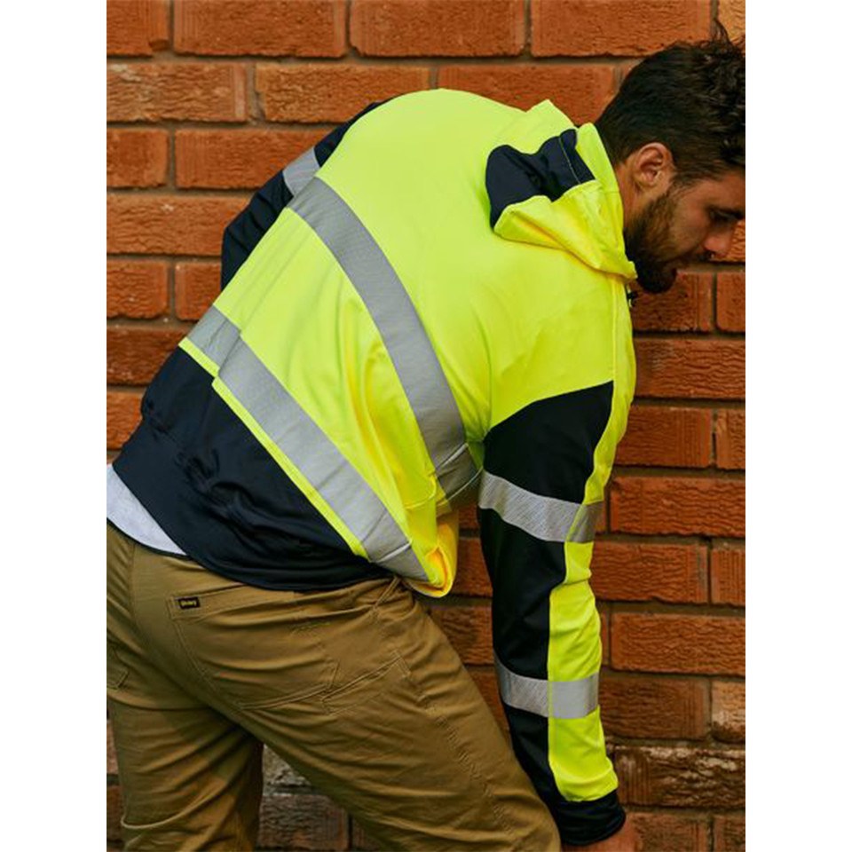 Man leaning against brick wall wearing fluoro yellow and navy hi vis hoodie with silver reflective tape