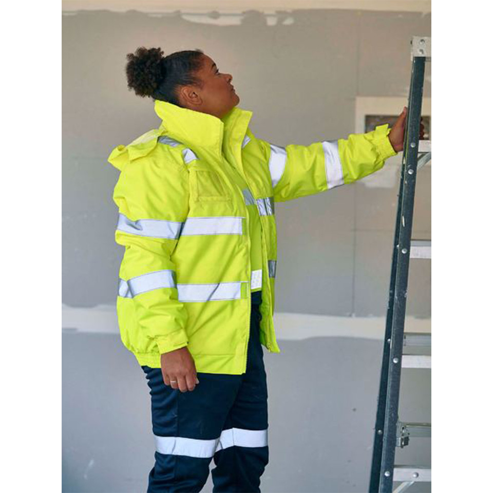 Woman on worksite wearing hi-vis yellow bomber jacket with silver reflective tape bands and raised collar