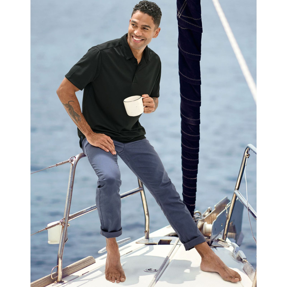 Man on sailboat wearing slate blue jean-style chino pants with rolled cuffs, paired with a black polo
