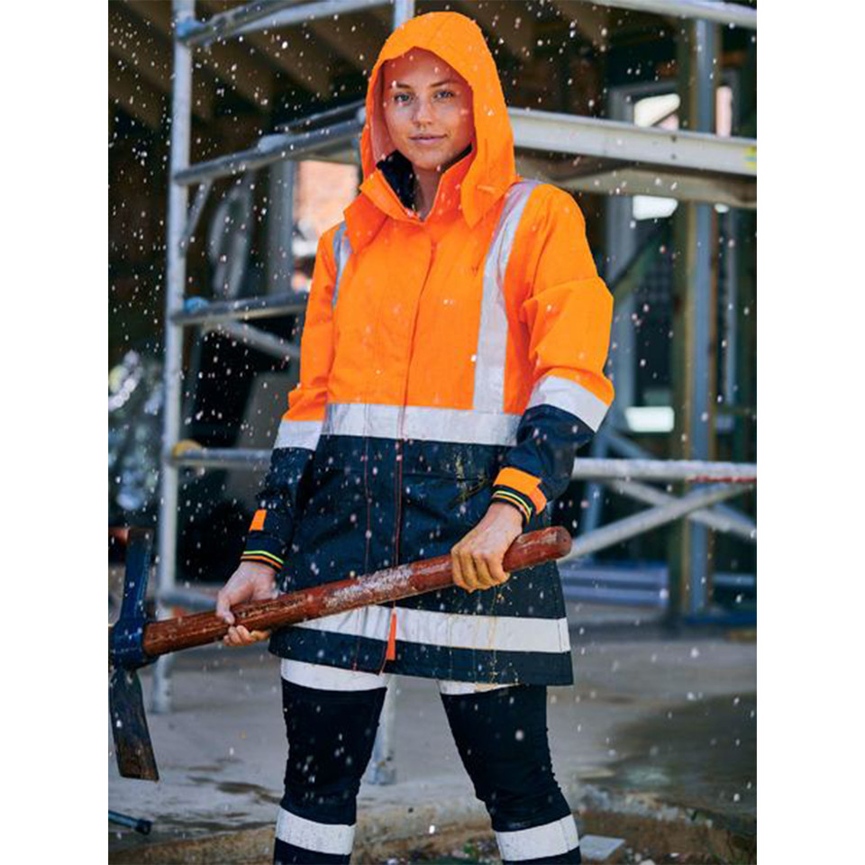 Woman on construction site wearing orange and navy hi vis rain jacket with hood up and reflective tape in rain